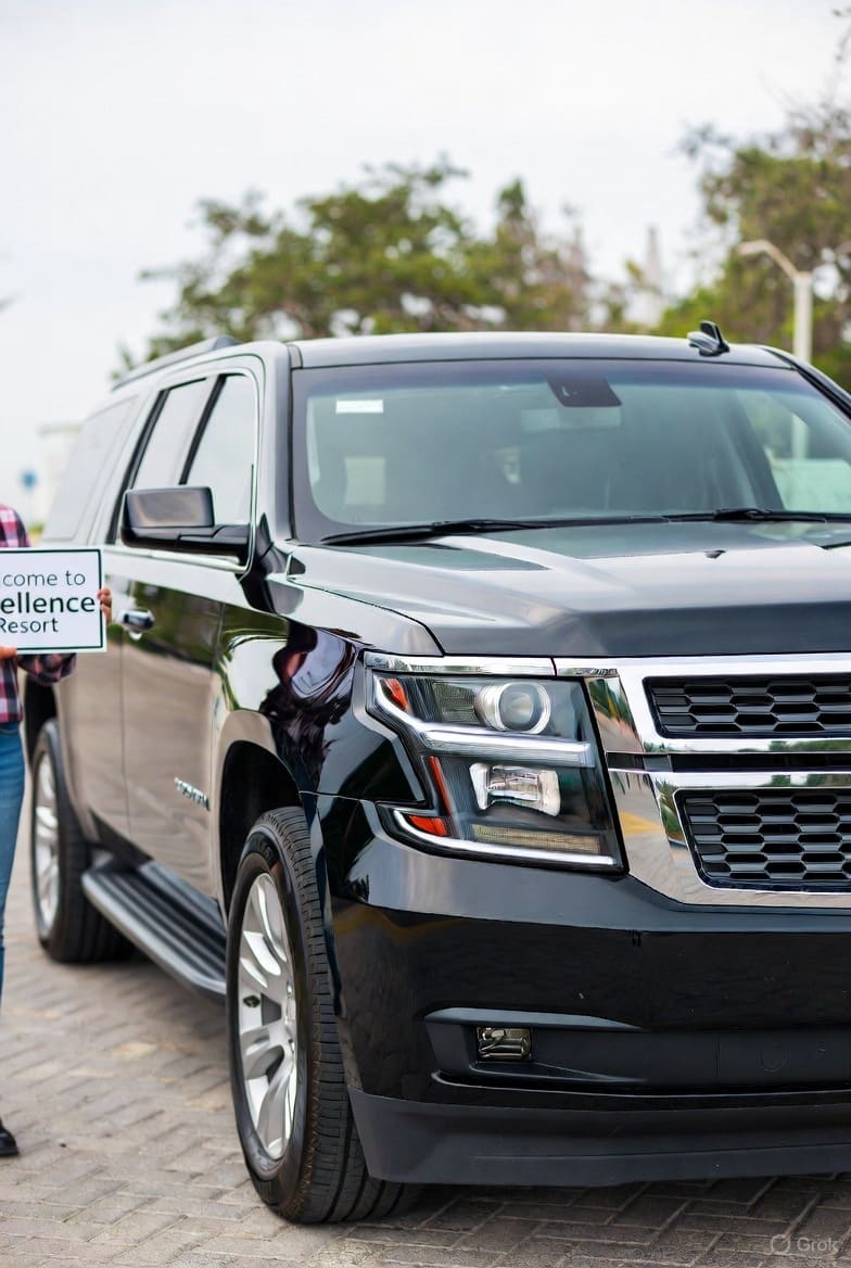 Private transfer Punta Cana airport to Excellence El Carmen – Black Chevrolet Suburban 2019 with driver and Welcome to Excellence Resort sign at PUJ arrivals